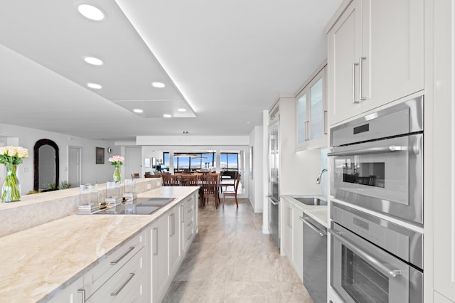 kitchen with sink, white cabinets, light stone counters, and appliances with stainless steel finishes