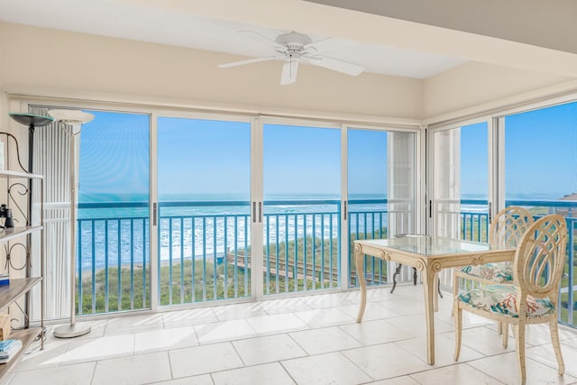 sunroom with ceiling fan, a water view, a view of the beach, and a wealth of natural light