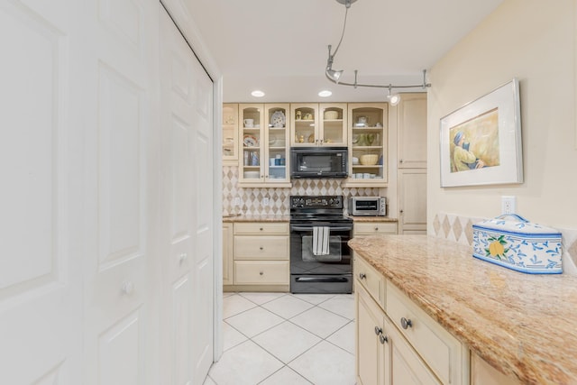 kitchen featuring cream cabinetry, black appliances, light tile patterned floors, light stone counters, and backsplash