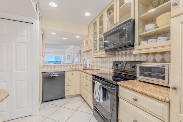 kitchen with cream cabinetry, black appliances, light tile patterned floors, light stone counters, and decorative backsplash