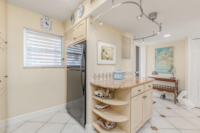 kitchen featuring light tile patterned floors, light stone counters, rail lighting, and stainless steel refrigerator