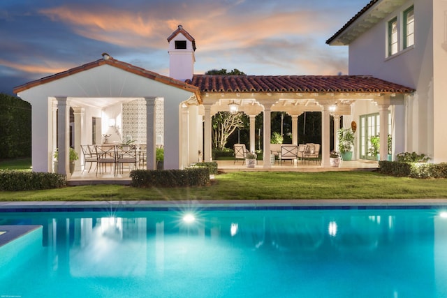 back house at dusk featuring a yard, an outdoor structure, and a patio