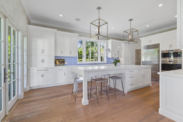 kitchen featuring pendant lighting, appliances with stainless steel finishes, light hardwood / wood-style floors, an island with sink, and white cabinets