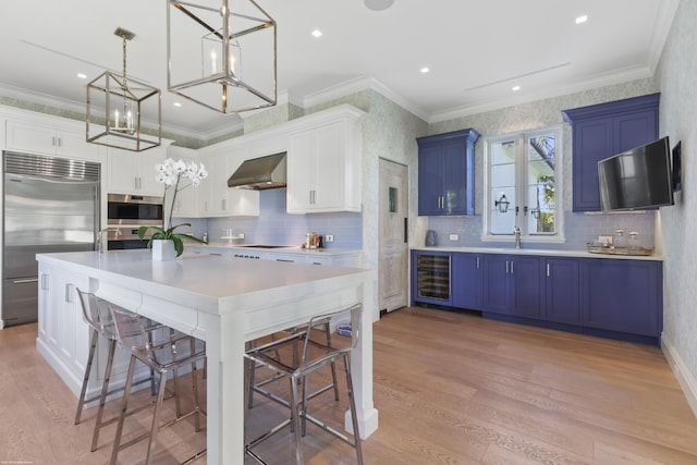 kitchen with blue cabinets, wall chimney range hood, white cabinets, and appliances with stainless steel finishes