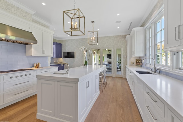 kitchen with sink, white cabinets, hanging light fixtures, ornamental molding, and a kitchen island with sink