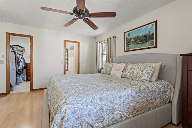 bedroom featuring a walk in closet, a textured ceiling, ceiling fan, light hardwood / wood-style flooring, and a closet