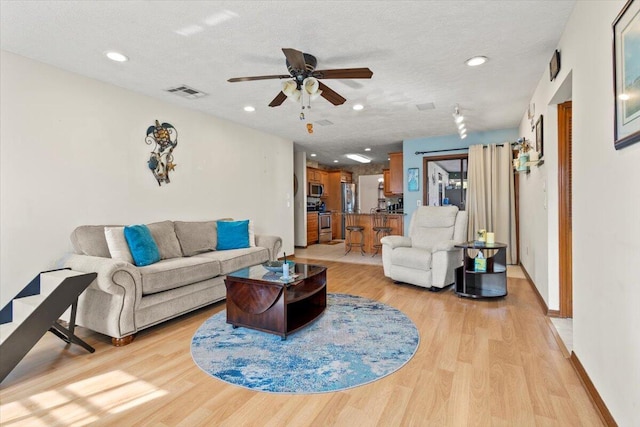 living room with a textured ceiling, light hardwood / wood-style floors, and ceiling fan