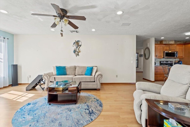 living room featuring ceiling fan, light wood-type flooring, and a textured ceiling