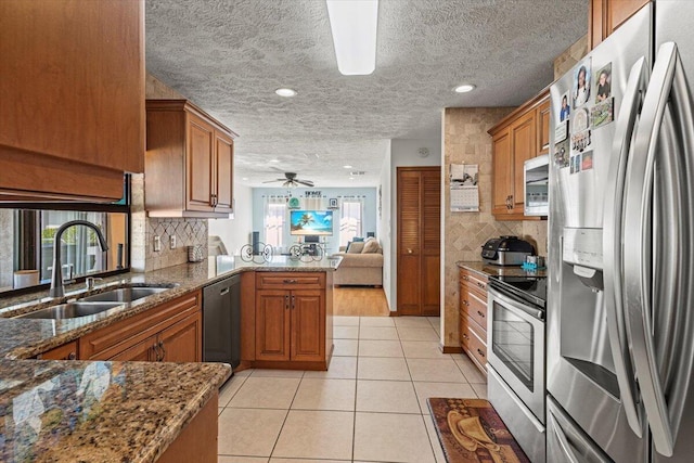 kitchen with ceiling fan, sink, stainless steel appliances, kitchen peninsula, and dark stone countertops