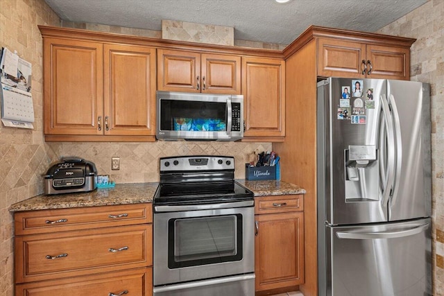 kitchen with backsplash, a textured ceiling, stainless steel appliances, and stone countertops