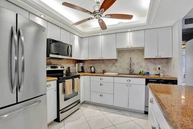 kitchen featuring stainless steel appliances, a tray ceiling, white cabinets, light tile patterned flooring, and sink