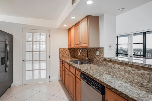 kitchen featuring light tile patterned floors, decorative backsplash, stone countertops, appliances with stainless steel finishes, and sink