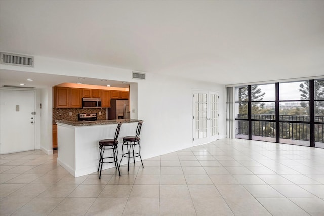 kitchen with a kitchen breakfast bar, light tile patterned floors, decorative backsplash, floor to ceiling windows, and appliances with stainless steel finishes