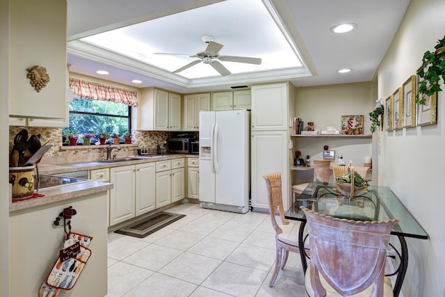 kitchen with white fridge with ice dispenser, a tray ceiling, backsplash, ceiling fan, and sink