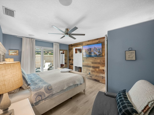 bedroom featuring access to exterior, ceiling fan, wood walls, light hardwood / wood-style floors, and a textured ceiling