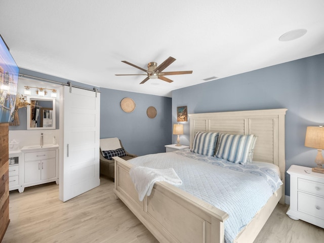 bedroom featuring a barn door, ceiling fan, ensuite bath, and light hardwood / wood-style floors