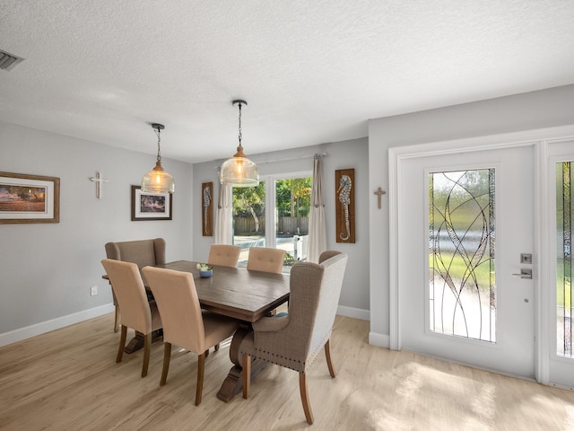 dining area with a textured ceiling, light hardwood / wood-style flooring, and a healthy amount of sunlight