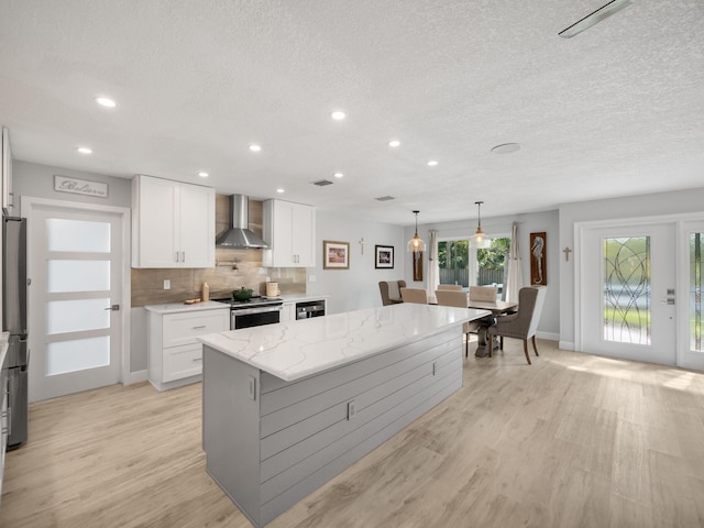 kitchen with white cabinetry, a center island, wall chimney range hood, decorative light fixtures, and stainless steel electric range