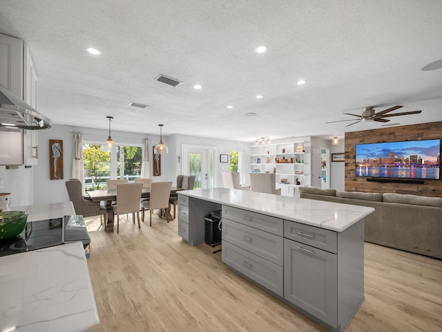 kitchen with light stone counters, a textured ceiling, gray cabinets, a kitchen island, and light wood-type flooring