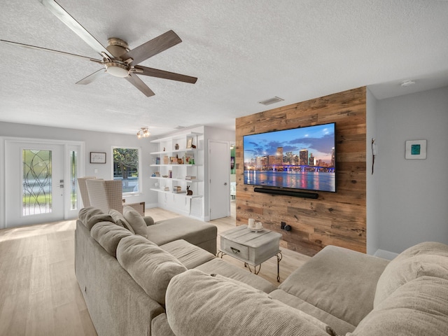 living room featuring wooden walls, light hardwood / wood-style flooring, ceiling fan, and a textured ceiling