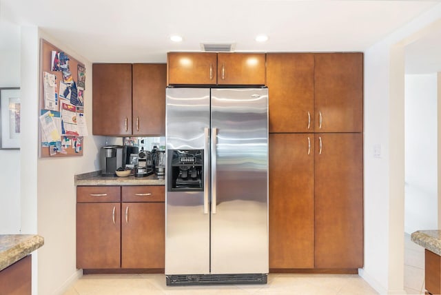 kitchen with light stone counters, stainless steel fridge, and light tile patterned flooring