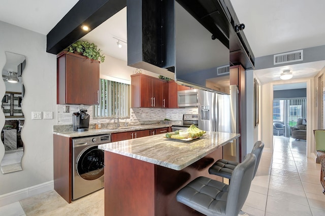 kitchen with washer / clothes dryer, appliances with stainless steel finishes, a breakfast bar, a kitchen island, and sink