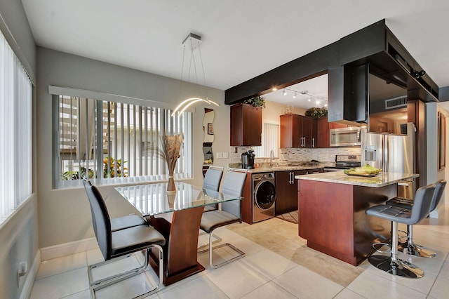 kitchen with pendant lighting, a center island, stainless steel appliances, decorative backsplash, and washer / dryer