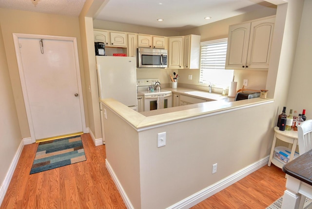 kitchen featuring sink, cream cabinets, white appliances, light wood-type flooring, and kitchen peninsula