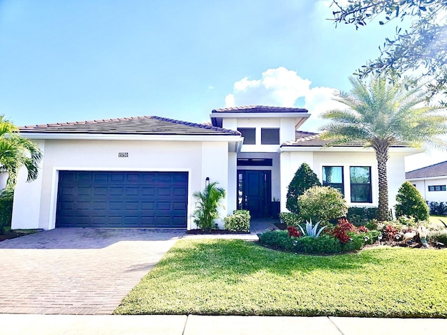 view of front facade featuring an attached garage, stucco siding, a front lawn, a tiled roof, and decorative driveway