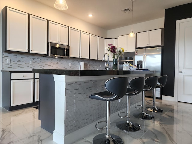 kitchen featuring a kitchen bar, visible vents, marble finish floor, decorative light fixtures, and stainless steel microwave