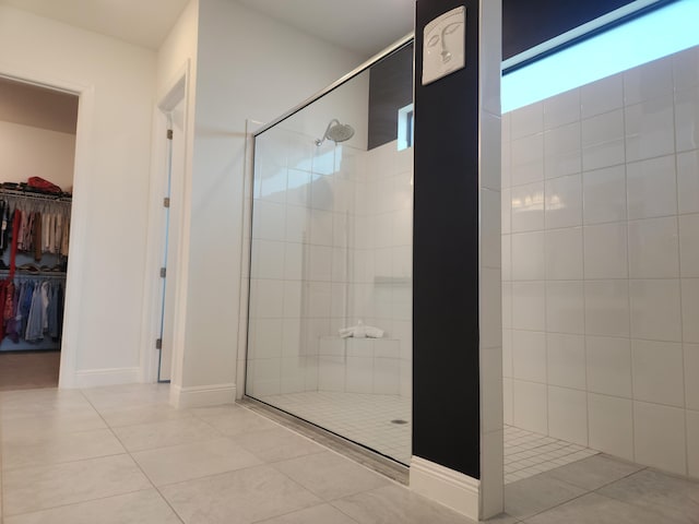 full bath with tile patterned floors, tiled shower, a walk in closet, and baseboards