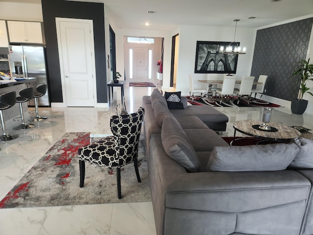 living room with baseboards, marble finish floor, an accent wall, and an inviting chandelier