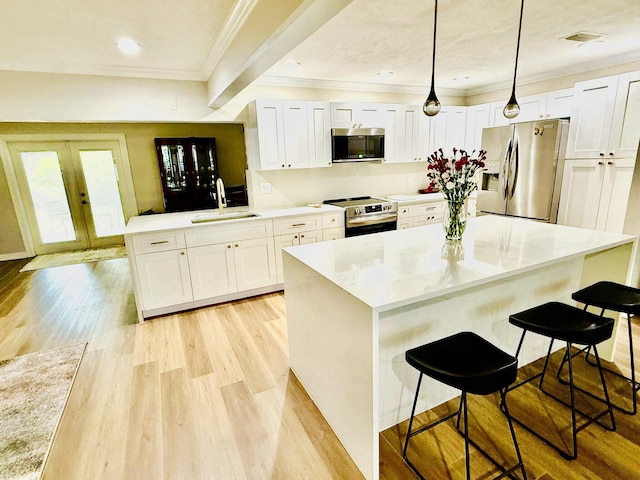 kitchen featuring sink, white cabinetry, hanging light fixtures, stainless steel appliances, and a kitchen bar