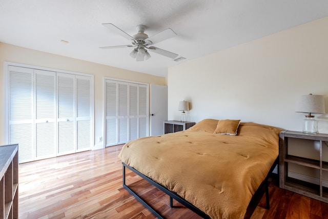 bedroom with hardwood / wood-style floors, ceiling fan, and multiple closets