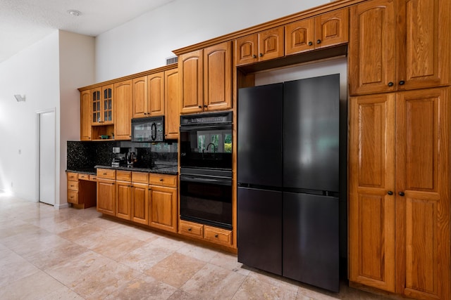 kitchen featuring decorative backsplash, a towering ceiling, dark stone countertops, and black appliances