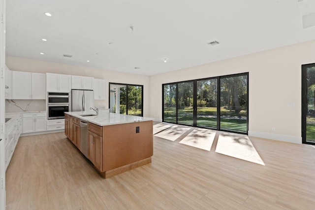 kitchen featuring white cabinetry, appliances with stainless steel finishes, backsplash, a kitchen island with sink, and light stone counters