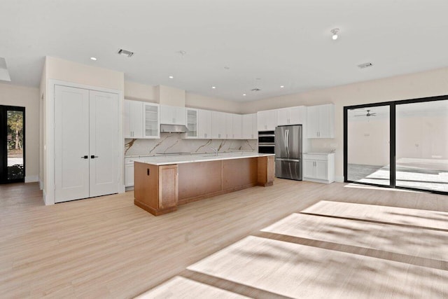 kitchen with white cabinetry, light hardwood / wood-style floors, appliances with stainless steel finishes, decorative backsplash, and a spacious island