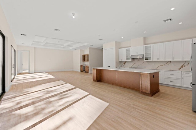 kitchen with white cabinetry, tasteful backsplash, light wood-type flooring, a large island with sink, and sink