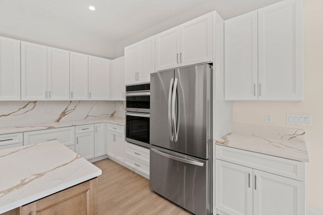 kitchen featuring light stone countertops, appliances with stainless steel finishes, white cabinetry, and light hardwood / wood-style floors