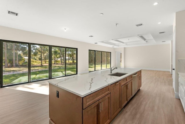 kitchen featuring a center island with sink, a raised ceiling, stainless steel dishwasher, light stone counters, and sink