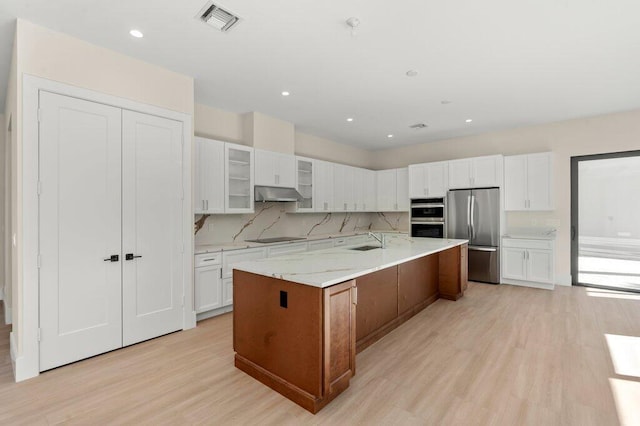 kitchen with white cabinetry, stainless steel appliances, sink, a large island, and light stone counters