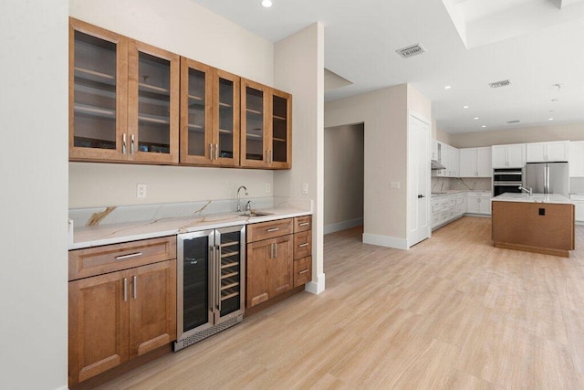 kitchen with wine cooler, a kitchen island, sink, appliances with stainless steel finishes, and light stone counters