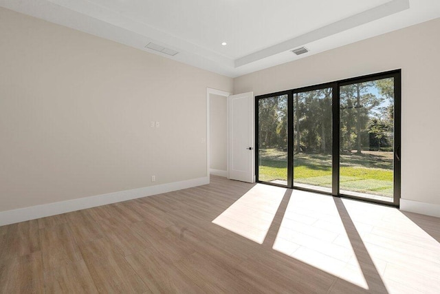 spare room with a tray ceiling and light hardwood / wood-style flooring