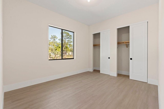 unfurnished bedroom with two closets and light hardwood / wood-style flooring