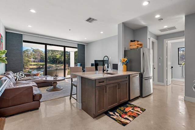 kitchen with sink, a kitchen island with sink, appliances with stainless steel finishes, a breakfast bar area, and dark brown cabinets