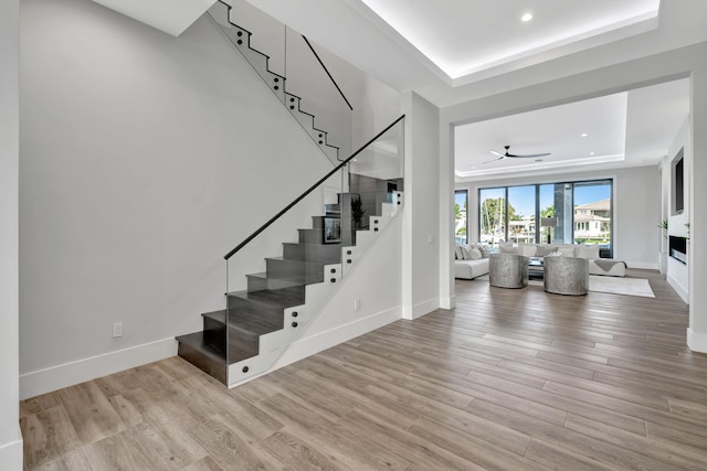 stairway with ceiling fan, a tray ceiling, and hardwood / wood-style floors