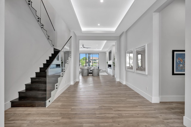 foyer with ceiling fan, a raised ceiling, and light wood-type flooring