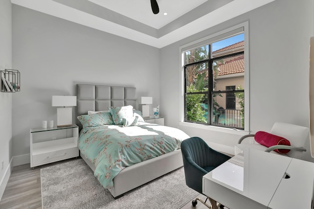 bedroom featuring ceiling fan, a raised ceiling, and light hardwood / wood-style flooring