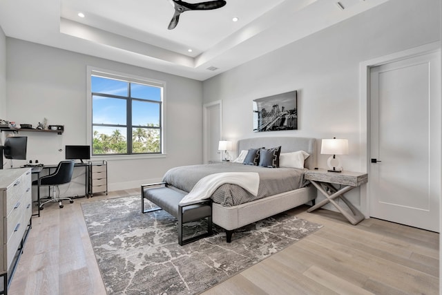 bedroom with ceiling fan, light hardwood / wood-style flooring, and a tray ceiling