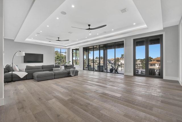 unfurnished living room with ceiling fan, light hardwood / wood-style floors, and a raised ceiling